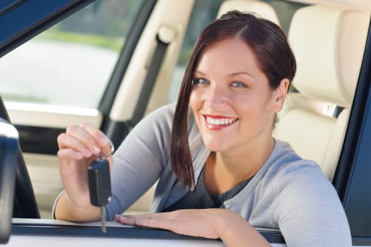 Attractive elegant businesswoman in new car showing keys smiling
