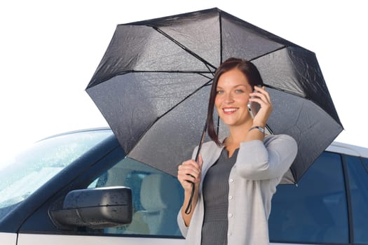 Attractive elegant businesswoman under umbrella by luxury car calling phone
