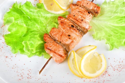 salmon kebab at plate with green lettuce and lemon on a white