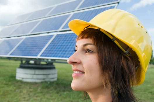 Side head portrait of a young brunette woman with yellow construction helmet as a headgear and optimistic view to the side