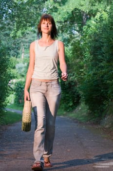 Border body view of a young dark-haired woman on a walkway in the park with a handbag carried casually