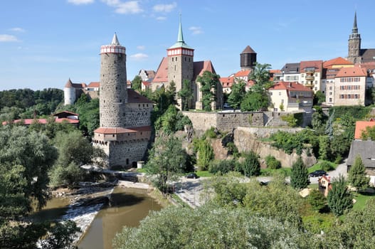 view of city center with ancient fortifications and city walls that surround houses, church, towers and lean over the river