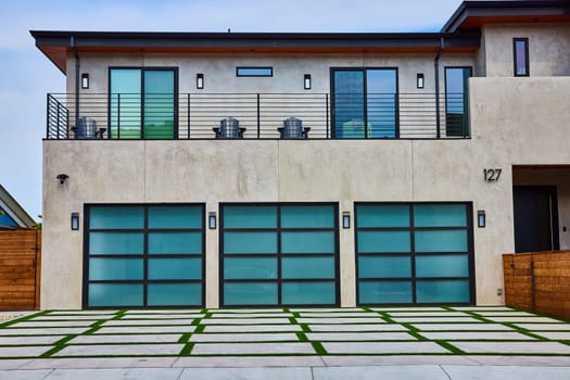 Image of Large mansion with three garage doors and fancy balcony over grass and stone driveway