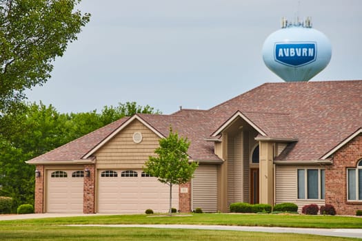 Image of Brown house with tan siding and garage door with reddish brown bricks and water tower in distance