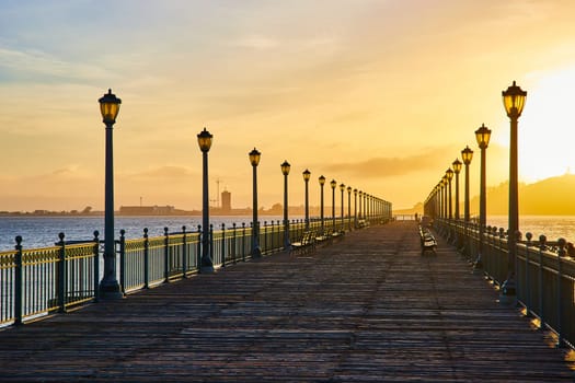 Image of Golden sunrise beside Pier 7 lined with benches and lamp posts in ocean water