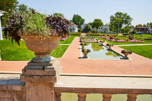 Image of Stone flower pot with green and purple plants on balcony overlooking pools of water and flowers