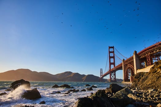 Image of Spray of water over partially submerged boulders on shoreline to Golden Gate Bridge