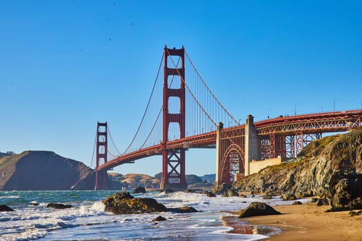 Image of Boulders on sandy beach with waves and seafoam on shoreline to Golden Gate Bridge