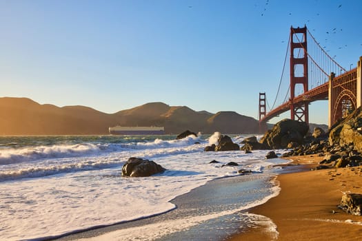 Image of Crashing wave near sandy beach with seagulls above Golden Gate Bridge