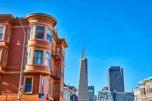 Image of Unique glossy orange house with round bay windows and fire escape with blue sky San Francisco