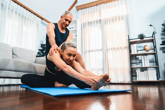 Happy active senior couple in sportswear being supportive and assist on yoga posture together at home. Healthy senior man and woman lifestyle with yoga exercise. Clout