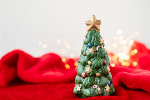 New Year's location with a green toy fir tree standing on a red blanket against a bokeh background with a garland of lights. Place for an inscription