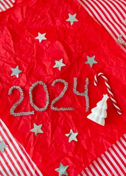 The inscription for the New Year 2024 on a red background along with a ceramic Christmas tree and a candy cane. Vertical photo