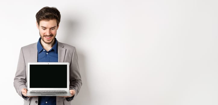 Handsome caucasian businessman in suit showing empty laptop screen, demonstrate promo, standing on white background.