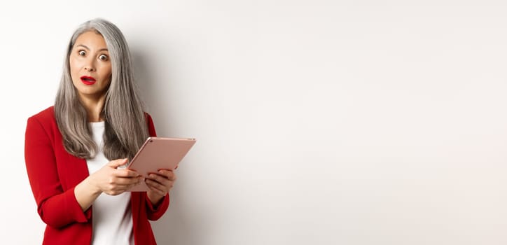 Business. Surprised asian businesswoman looking impressed after reading something on digital tablet, standing over white background.