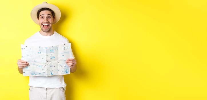 Travelling, vacation and tourism concept. Excited man tourist going sightseeing with map, standing over yellow background.