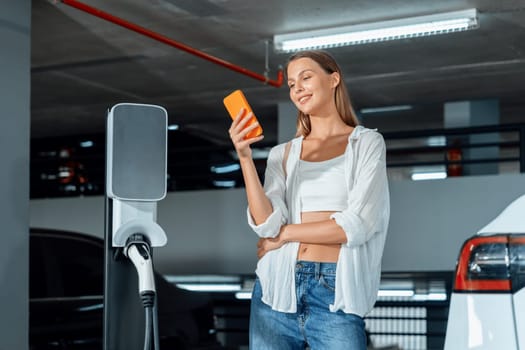 Young woman travel with EV electric car to shopping center parking lot charging in downtown city showing urban sustainability lifestyle by green clean rechargeable energy of electric vehicle innards