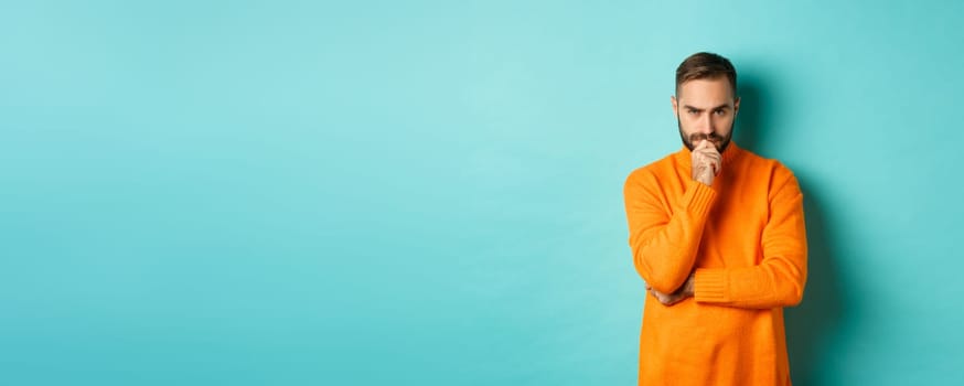 Thougtful young man making decision, looking serious and thinking, choosing, standing near copy space turquoise background.