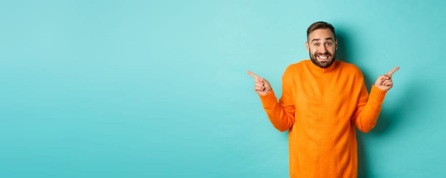 Confused handsome man shrugging indecisive, pointing fingers sideways, cant choose between two variants, standing against light blue background.