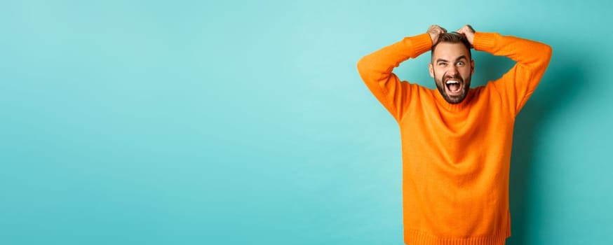 Frustrated man shouting, pulling out hair and screaming angry, losing temper and looking mad, standing over light blue background.