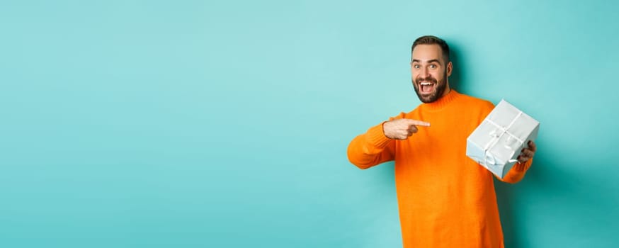 Holidays and celebration concept. Excited man receiving gift, looking happy at present and smiling, standing over blue background.