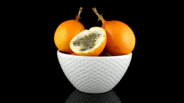 Passion fruit maracuja granadilla on ceramic white bowl, black background.