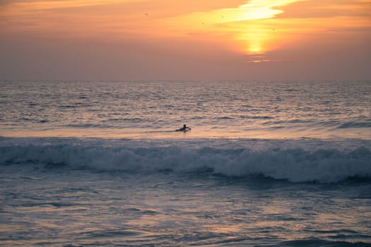 Surfer silhouette in the Atlantic Ocean from Furadouro Beach at sunset and golden hour, Ovar - Portugal.