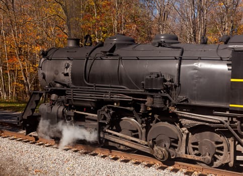 Old steam locomotive pulls freight through rural countryside in autumn