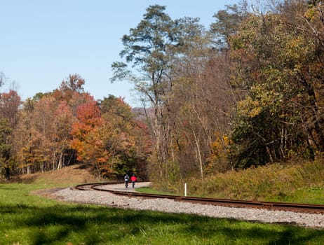 Two cyclists ride bikes down besides old railway line in rural countryside