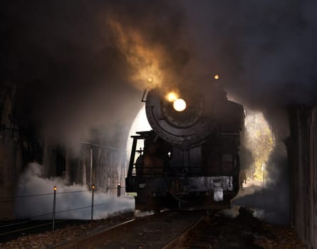 Old steam train pulling into a tunnel belching steam and smoke