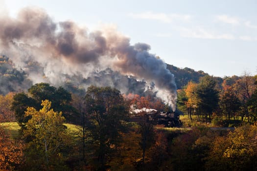 Old steam locomotive pulls freight through rural countryside in autumn