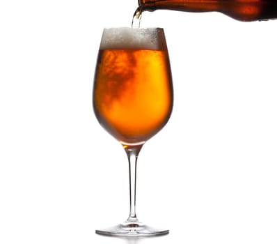 Chilled isolated beer goblet with small droplets of condensation on the outside of the glass and filled with golden colored beer being poured from brown bottle
