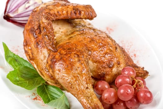 Half roasted chicken closeup with grape and greens on a white