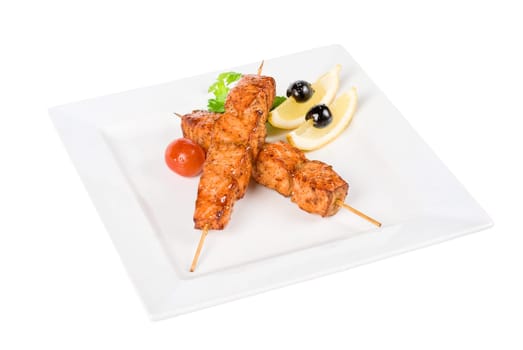 salmon kebab at plate with green lettuce and lemon on a white