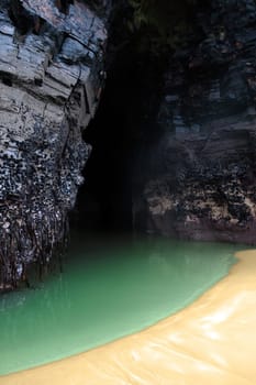 a beautiful green pool on sandy beach against cliffs