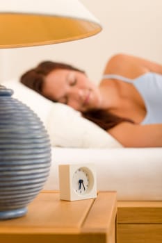 Alarm clock on bedside table woman sleeping in white bed