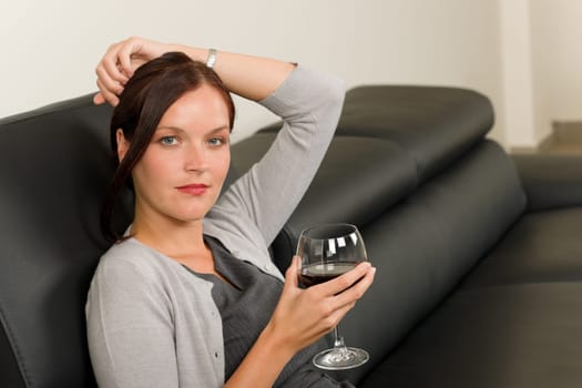 Elegant businesswoman sitting on leather sofa drink glass red wine