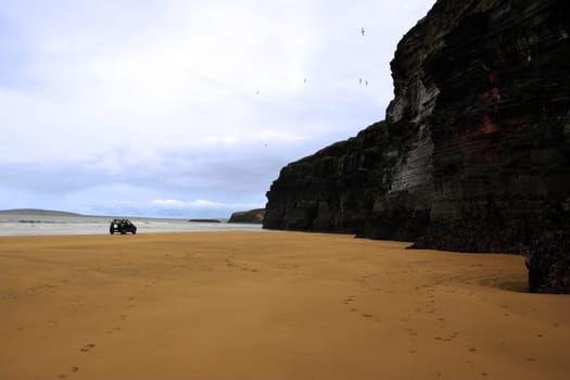 four wheel drive car on ballybunion beach with cliffs in background
