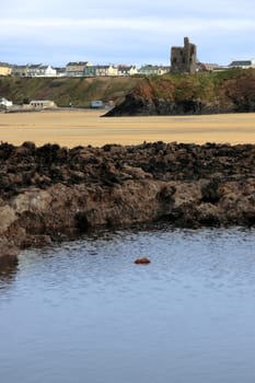 the old ruin of a castle in ballybunion overlooking the beach with black rocks in foreground