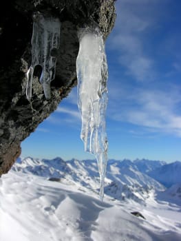 Icicle on a rock among snow-covered mountains