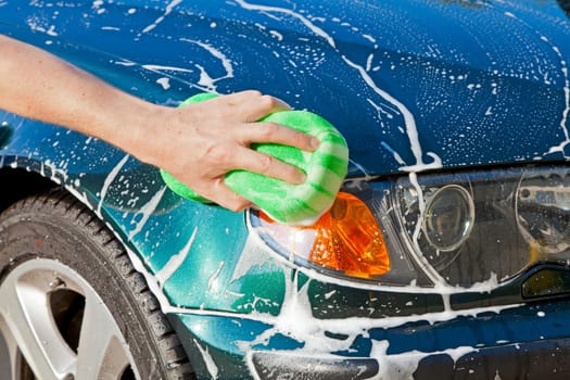 Closeup image of a hand with a soapy sponge washing a vehicle