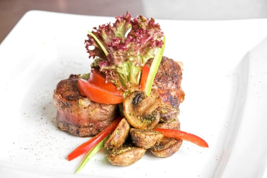 Tasty beef steak grilled in a cast-iron ribbed fry pan with bacon decorated with vegetables and roasted mushrooms