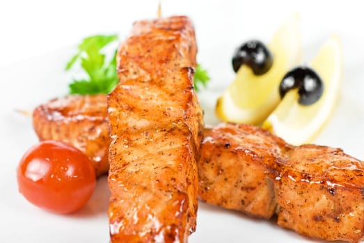 salmon kebab at plate with green lettuce and lemon on a white