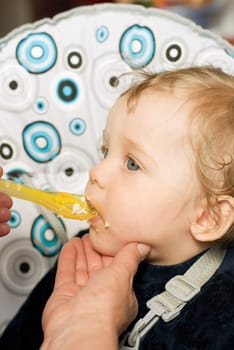 Baby boy feeding with a spoon at mum hand