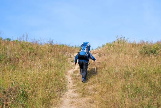 Hiker with rucksack up-hill at summer sunny day