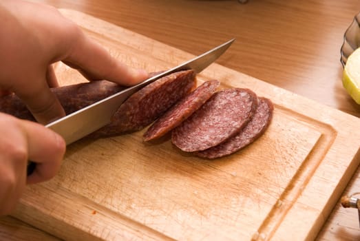 Hand closeup cuts salami with slice pieces at table