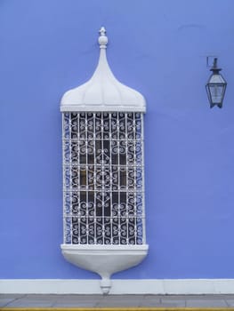 A spanish style white window grill against a blue wall.