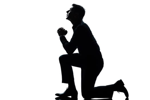one caucasian man kneeling praying  full length silhouette in studio isolated white background