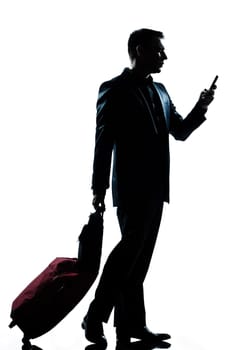 one caucasian business traveler man walking with telephone and  suitcase  full length silhouette in studio isolated white background