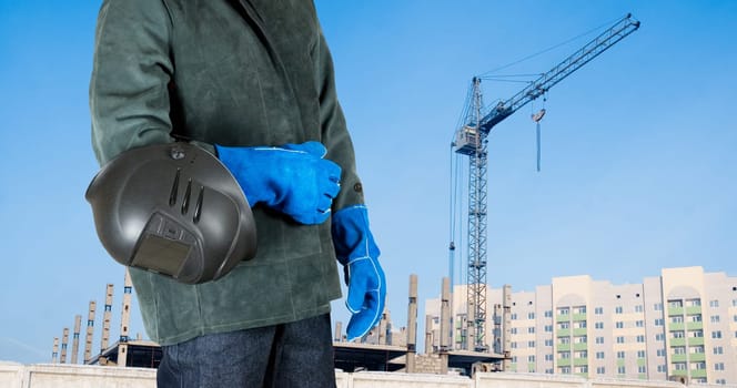 male welder closeup with welding equipment on building background